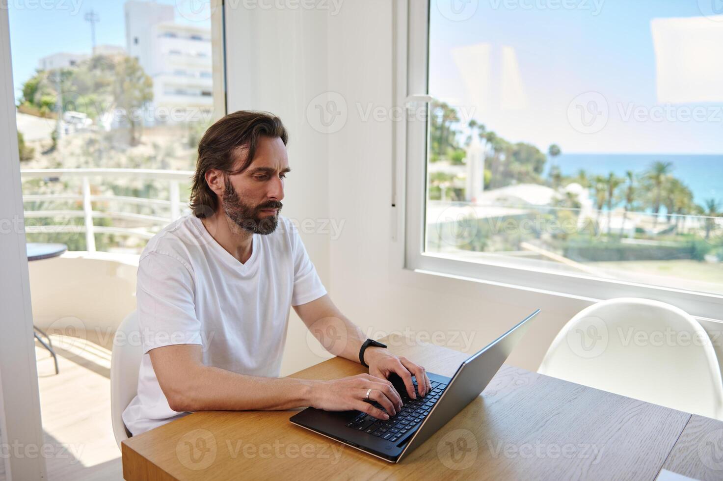 Bearded Young Man Working Remotely at Home with Scenic Ocean View Background photo