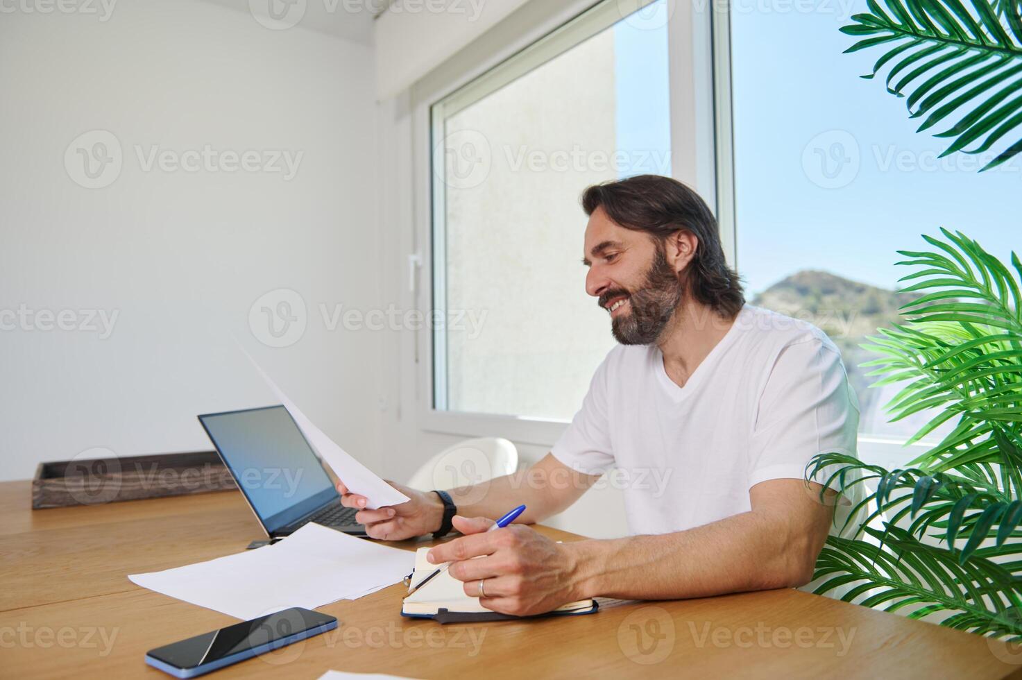 Bearded Man Working Remotely From a Bright Home Office Desk With Digital Equipments photo