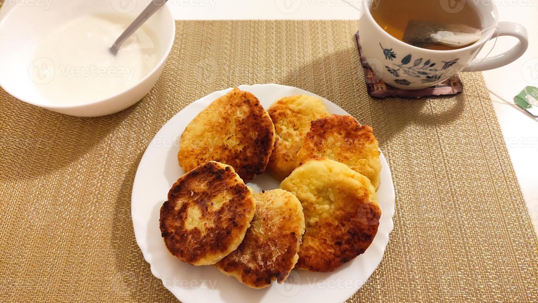 Syrniki, cottage cheese pancakes with sour cream and tea on tablecloth for breakfast photo