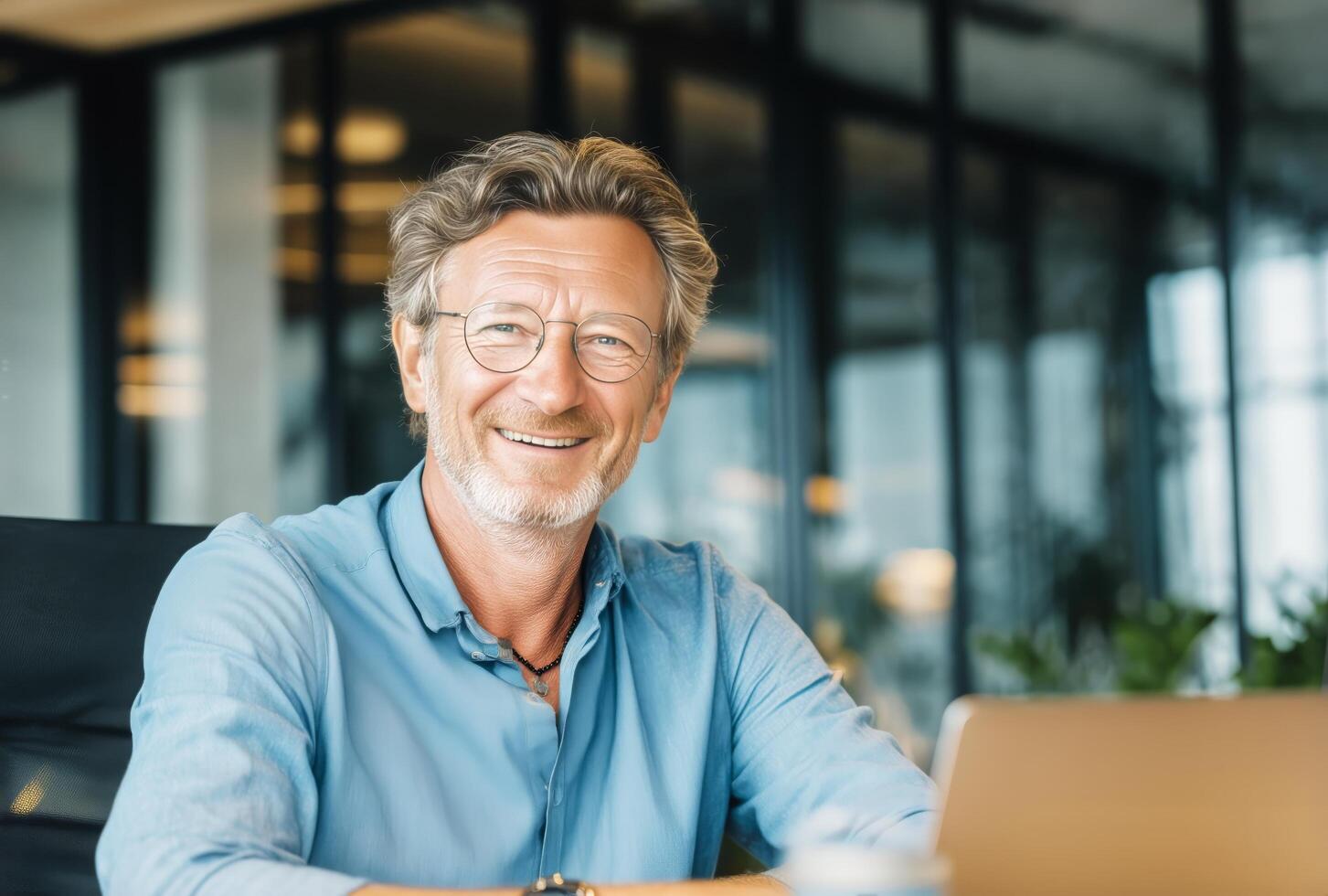A smiling man in a blue shirt sitting at a desk with a laptop photo
