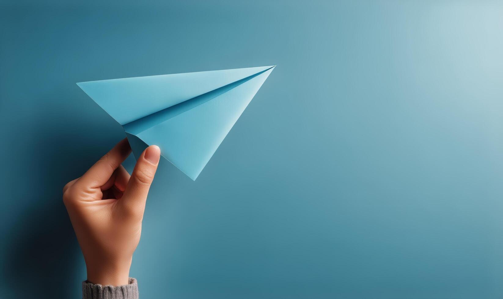 A person holding a paper airplane over a blue background photo