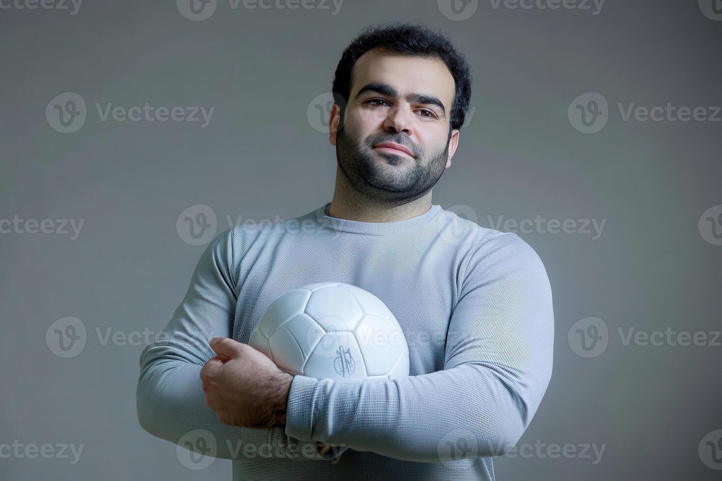 Portrait of a Man with a Soccer Ball A Strong and Confident Athlete Holding a White Soccer Ball Against a Grey Background photo