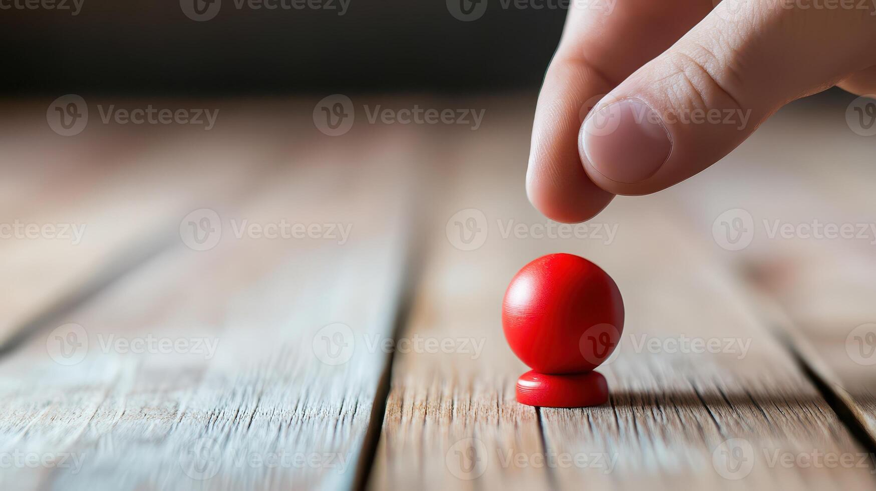 Hand positioning a red piece on a wooden surface photo