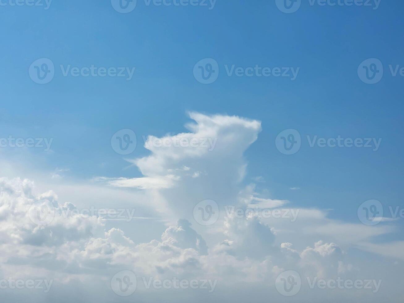 There are white cumulus clouds in the blue sky, one cloud looks like a running rabbit with ears photo