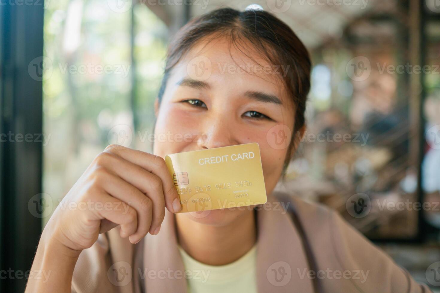 A cheerful woman displays a credit card in a sunlit cafe, highlighting modern lifestyle and financial themes. photo