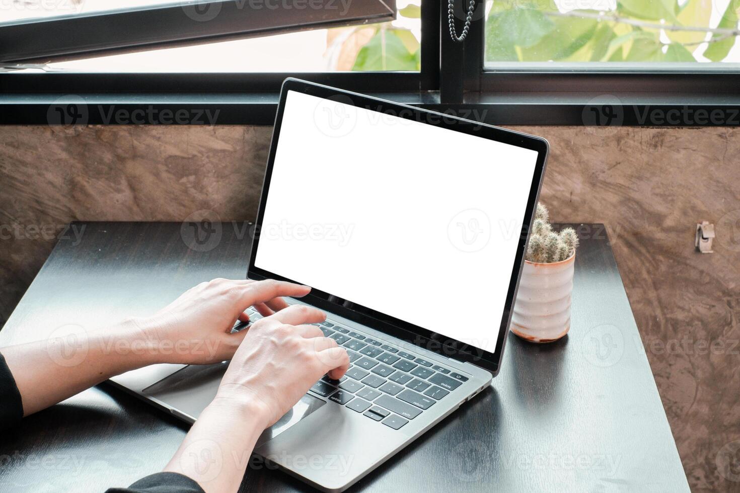 Hands typing on a laptop with a blank screen in a modern workspace by a window, featuring natural light and minimalist decor. photo