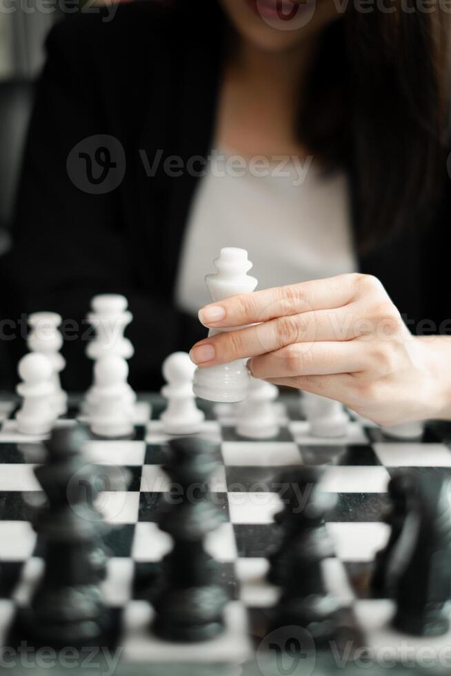A woman playing chess, focusing on moving a white piece on a classic black and white board, highlighting strategy and concentration. photo