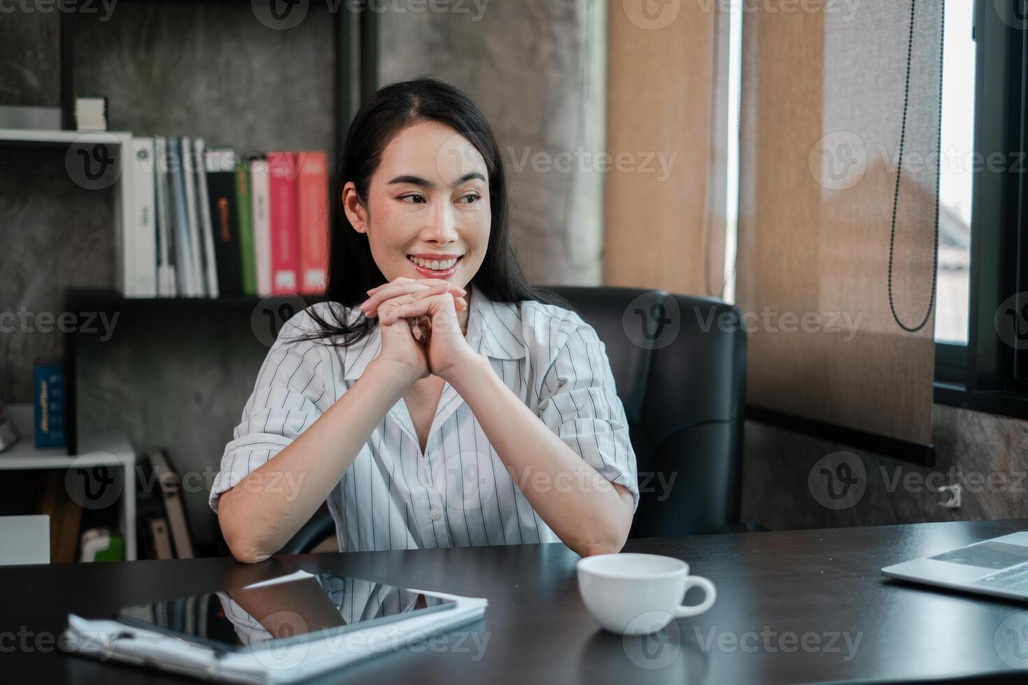 Businesswoman in a modern office, smiling while sitting at a desk with a tablet and coffee cup. photo