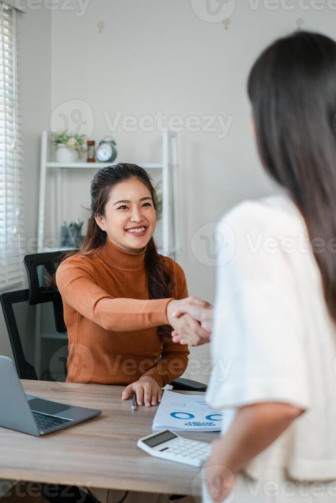 Two women engage in a professional handshake during a business meeting in a contemporary office environment. photo