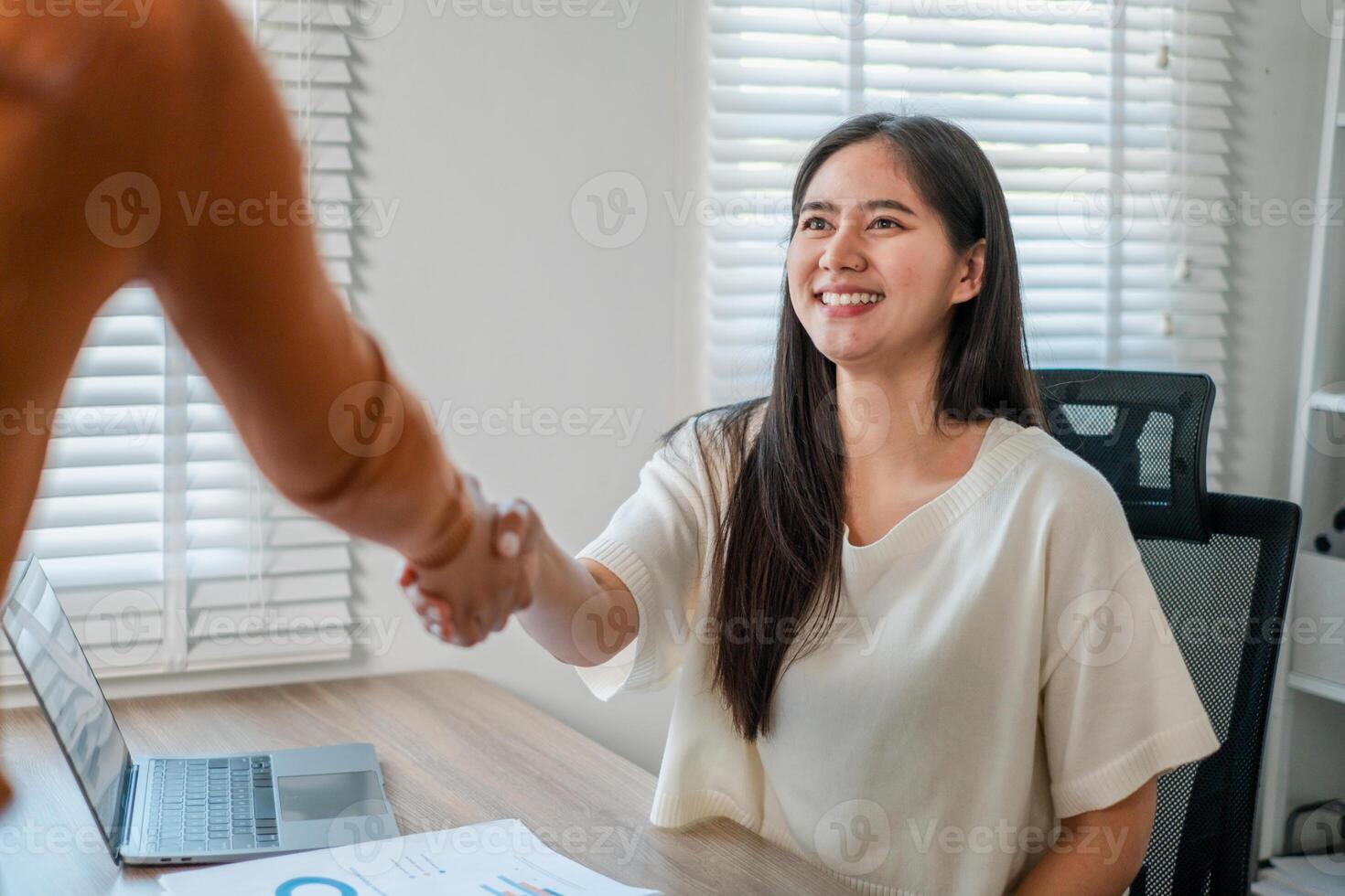 Smiling businesswoman shaking hands in a bright office, symbolizing successful partnership and collaboration. photo