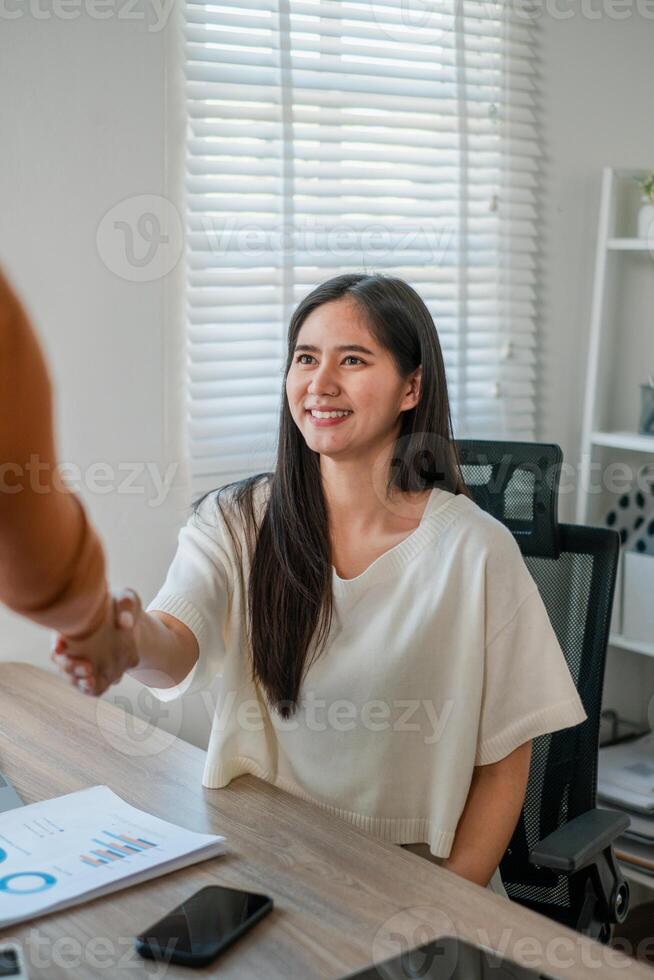 Businesswoman in a modern office, smiling and shaking hands, with documents and smartphone on the desk. photo