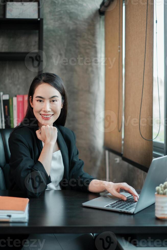 Businesswoman in a modern office, smiling confidently while working on a laptop, showcasing professionalism and success. photo