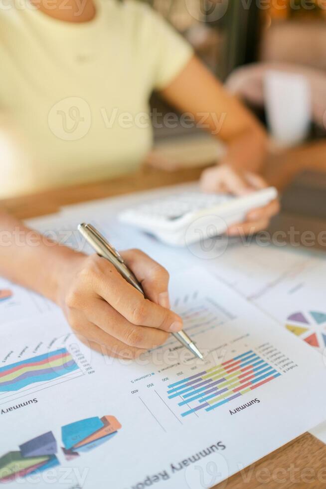 Close-up of a woman reviewing financial charts with a pen and calculator, focusing on data analysis and business strategy. photo