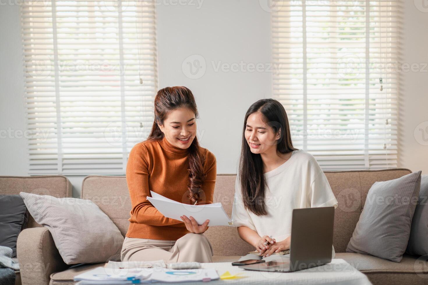 Two women discussing documents in a bright living room, showcasing teamwork and collaboration in a comfortable setting. photo