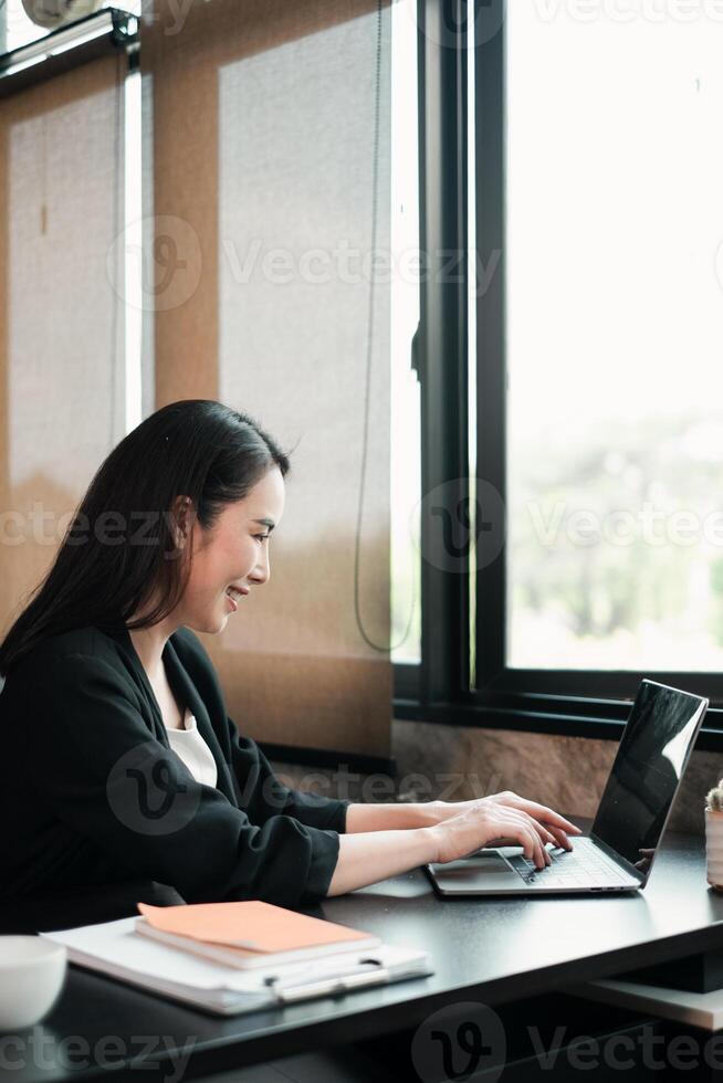 A focused woman using a laptop in a bright, modern office setting with large windows and natural light. photo