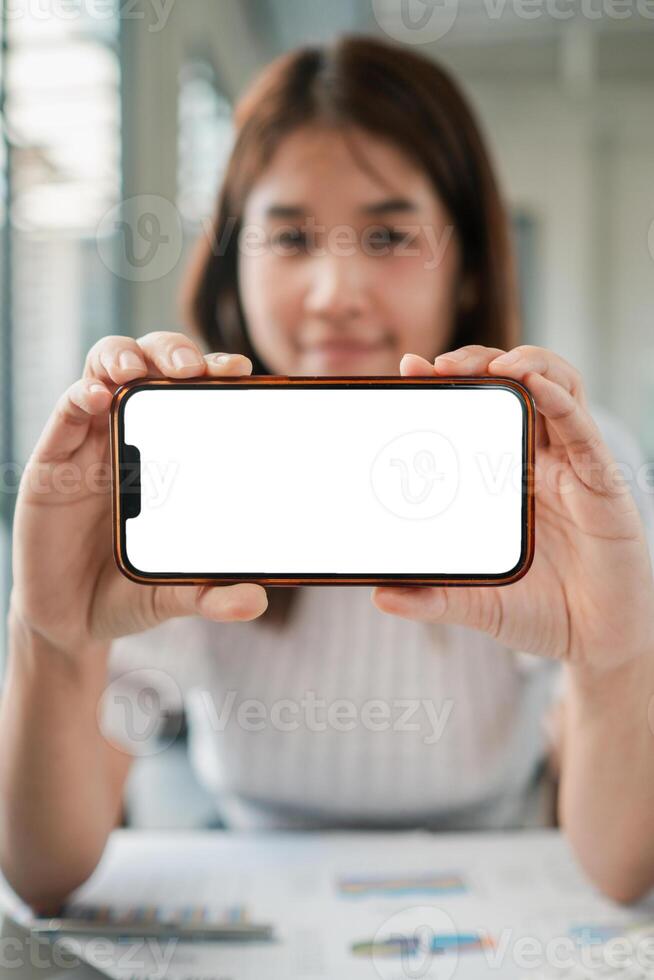Young woman displaying a smartphone with a blank screen, ideal for mockups or app presentations in a modern office setting. photo