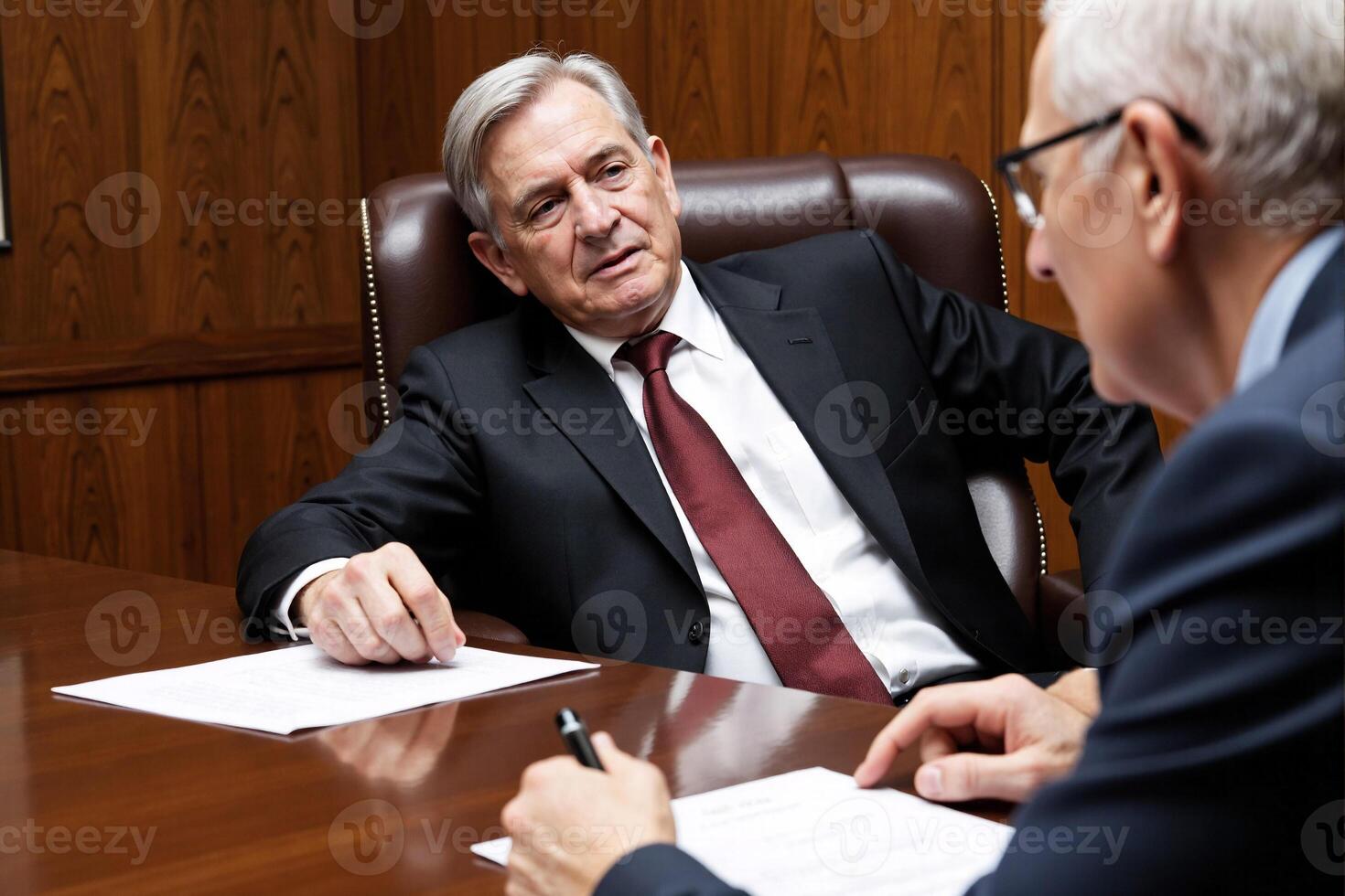 A man in a suit and tie sitting at a desk with another man photo