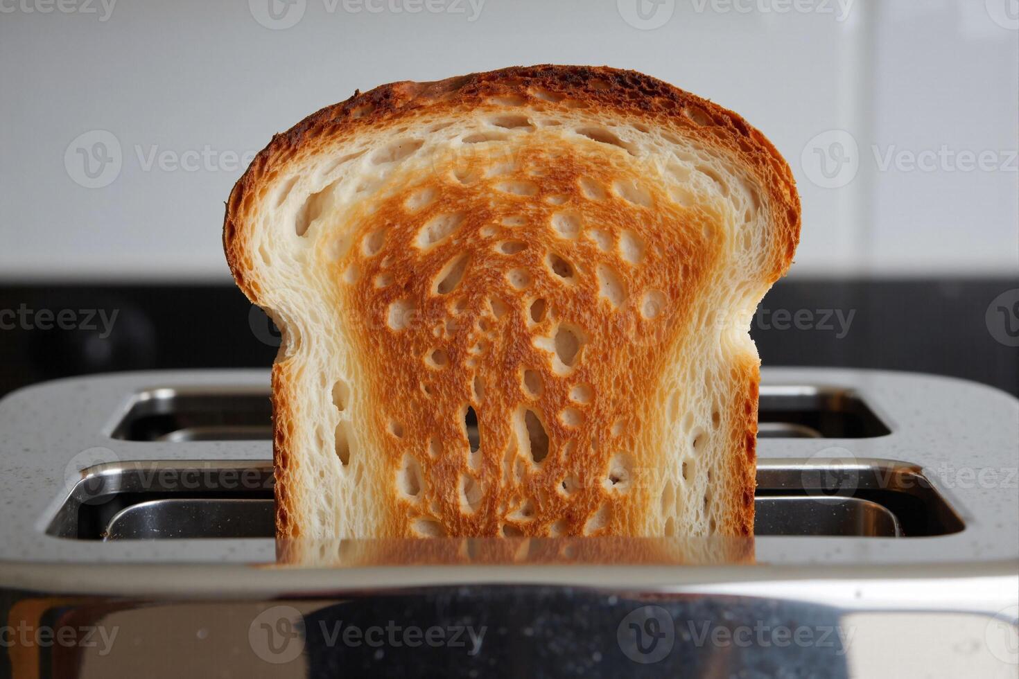 Perfectly toasted white bread slice emerging from stainless steel toaster with golden-brown crisp surface and visible soft interior, capturing everyday breakfast moment photo
