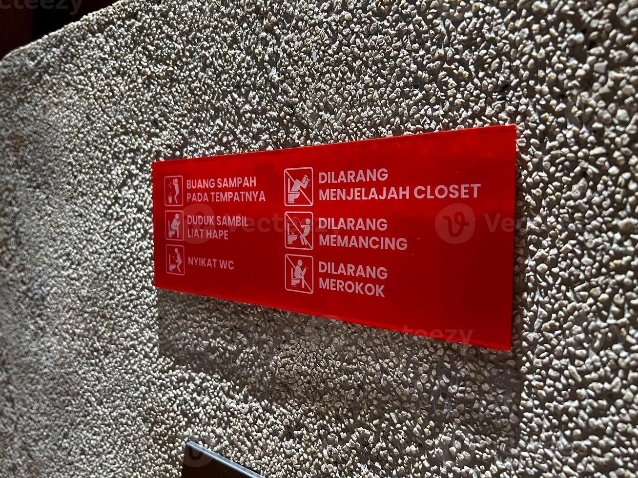 A prominently displayed red sign affixed to a wall displays several prohibitions in Indonesian Toilet photo