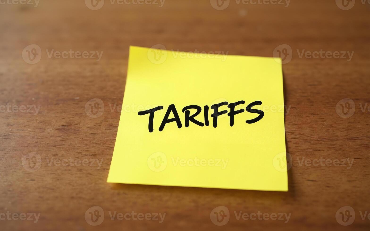 Tariffs reminder yellow sticky note with the word TARIFFS handwritten in black on a wooden surface, Trade tension concept photo