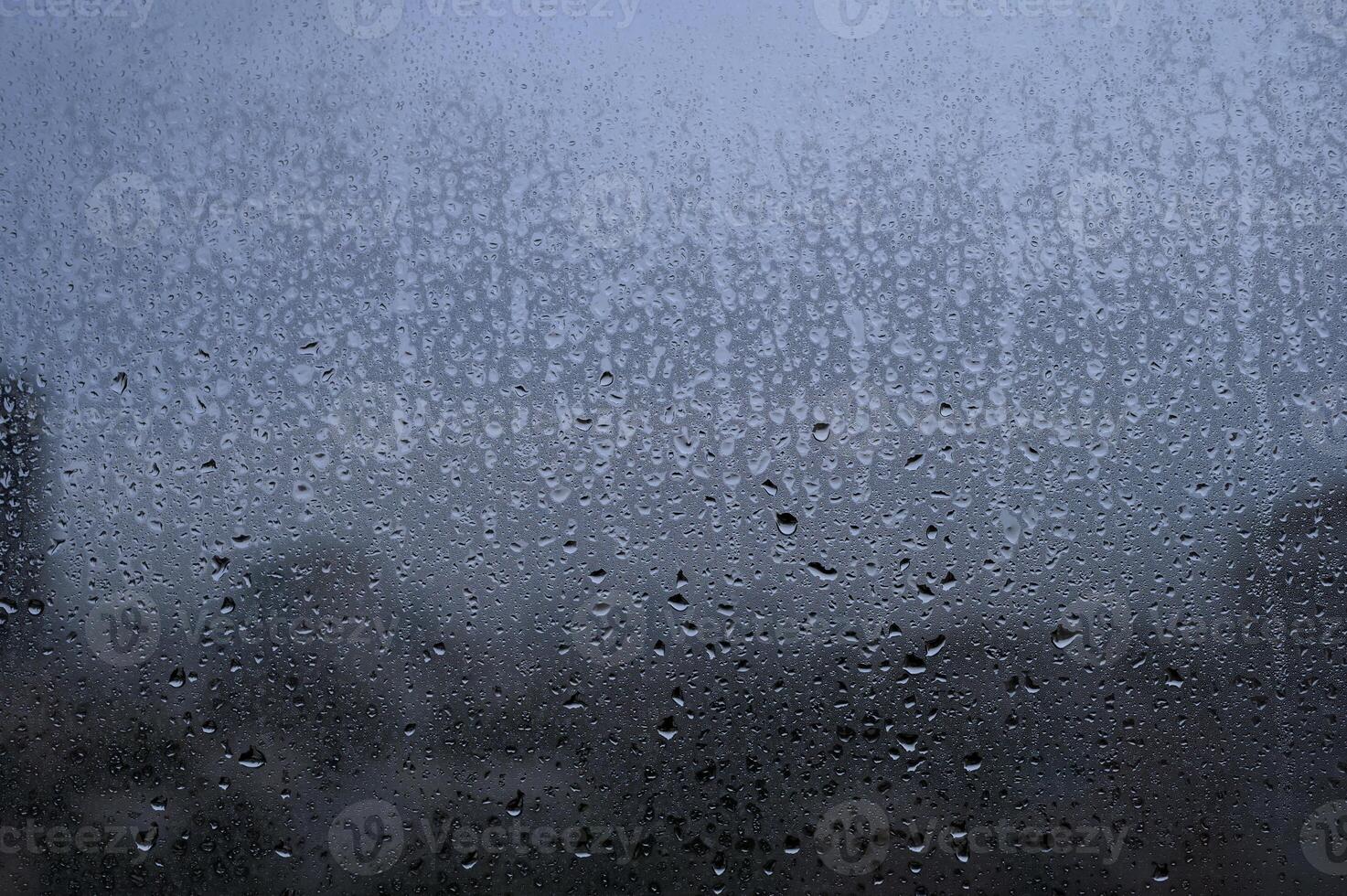Raindrops on a glass window with a blurry cityscape in the background on a cloudy day. photo