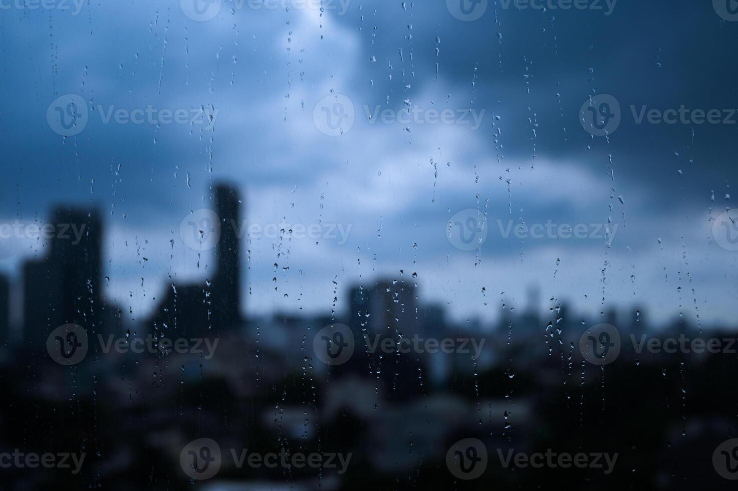 Raindrops on a window with a blurry city skyline in the background under a cloudy sky. photo