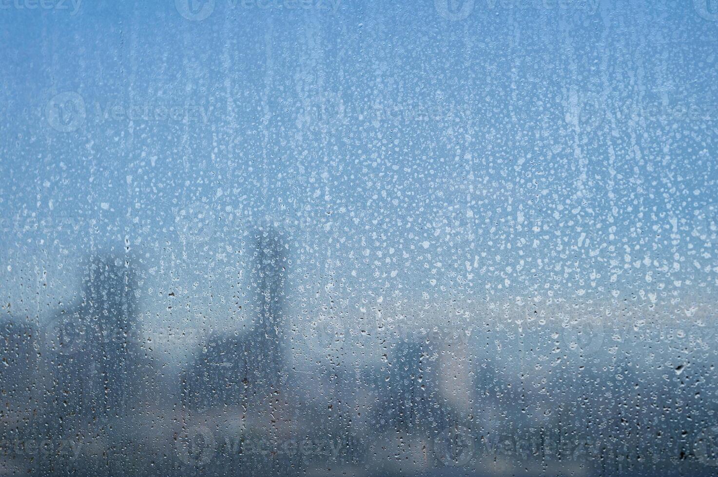 Raindrops on a glass window with a blurry cityscape in the morning background. photo