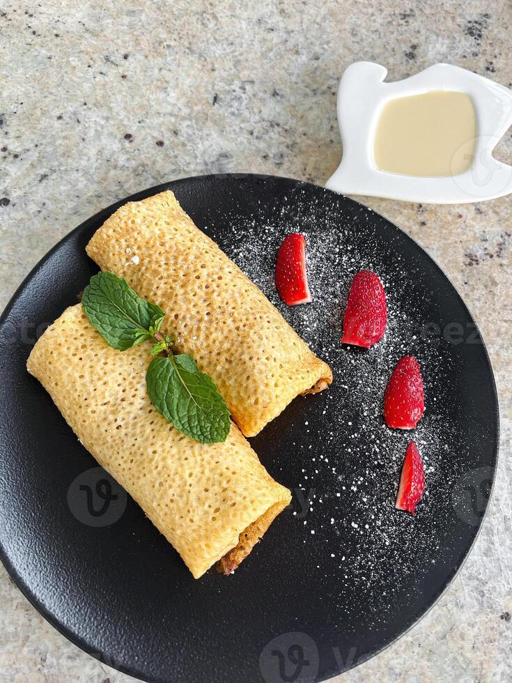 Rolled Pancakes with Strawberries. Crepes served with sweet condensed milk and berries photo