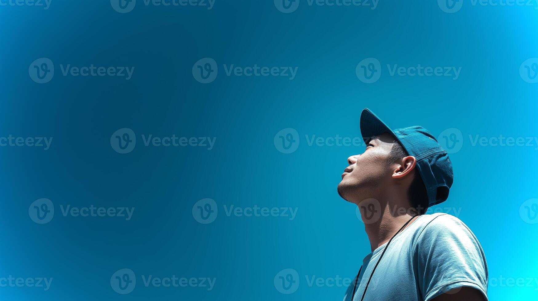 A young man stands in profile, looking up at a vibrant blue sky, exhibiting a sense of wonder and curiosity amidst a serene outdoor setting. photo