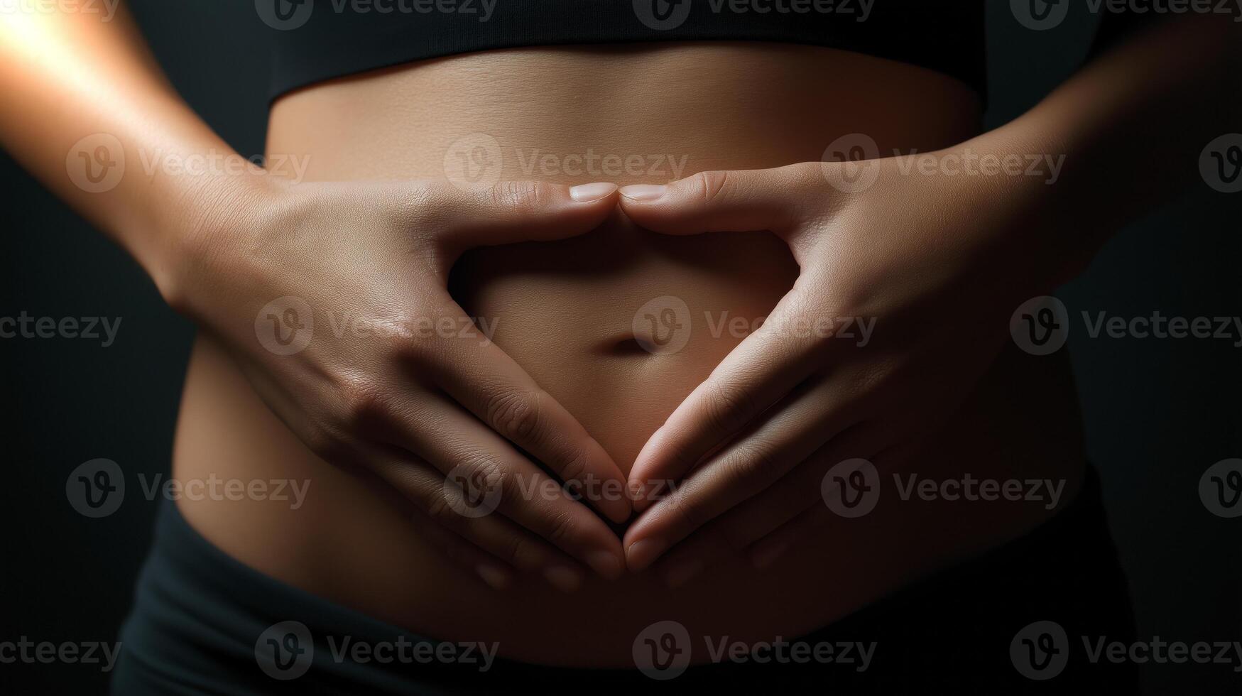 Two hands gently form a heart shape around a pregnant belly, symbolizing love and the joy of motherhood. The soft lighting enhances the intimate moment. photo
