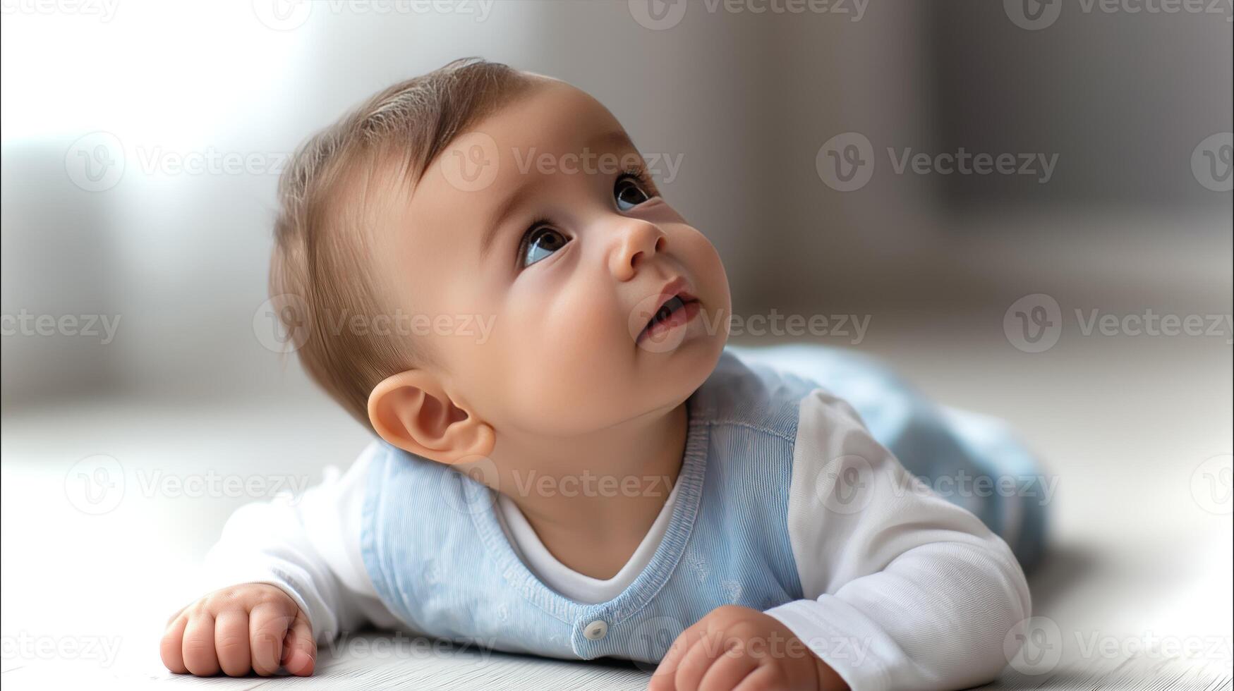 A baby is on its stomach, gazing up with wide, curious eyes in a softly lit room. The child seems curious and engaged, reflecting innocence and wonder. photo