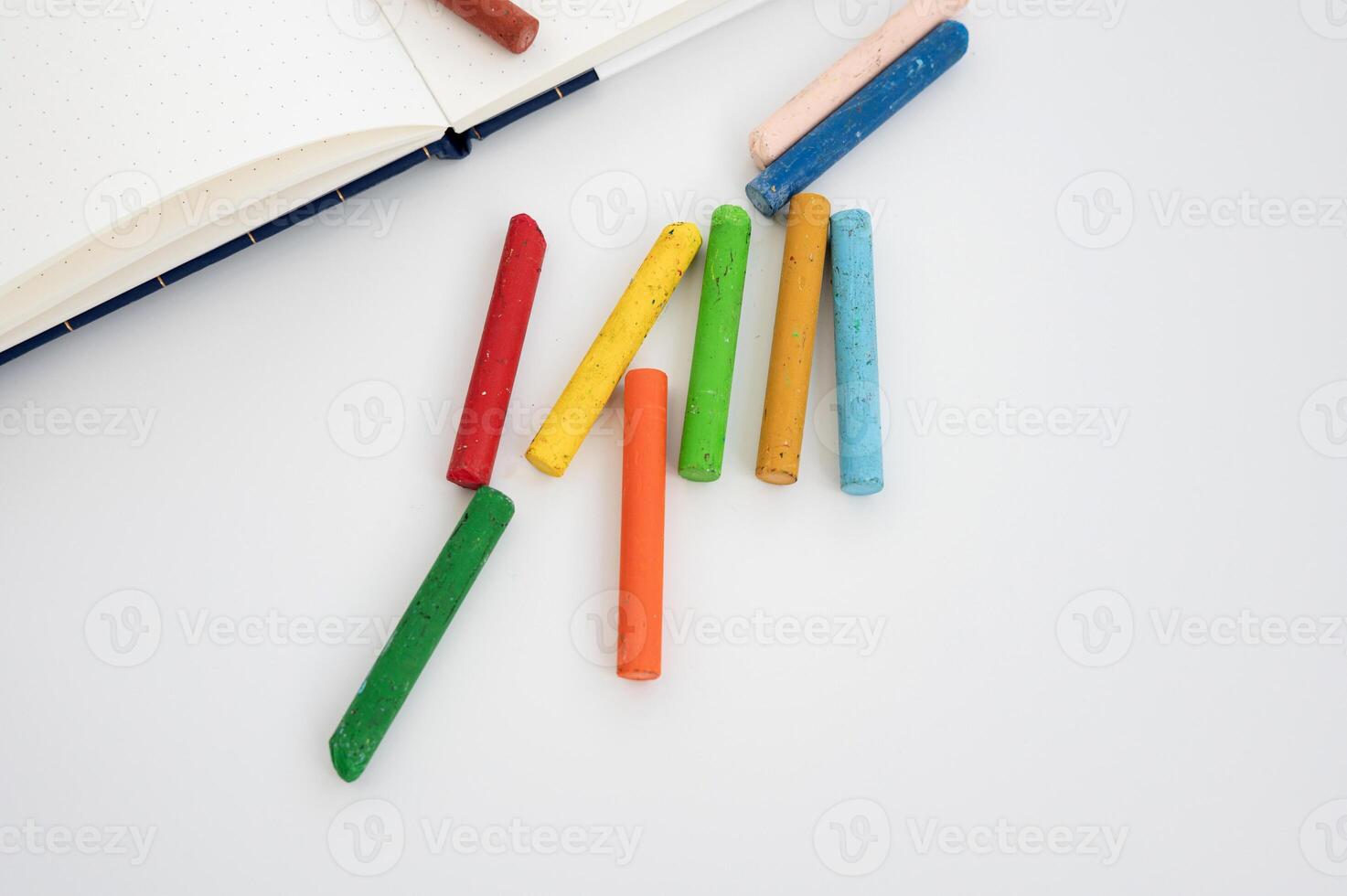 Colorful chalk sticks on white surface next to open notebook. Crayola Crayon Day photo