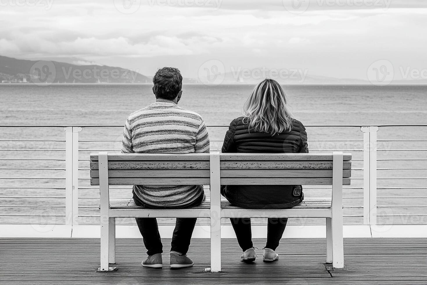 A couple sitting on a bench looking out at the ocean photo