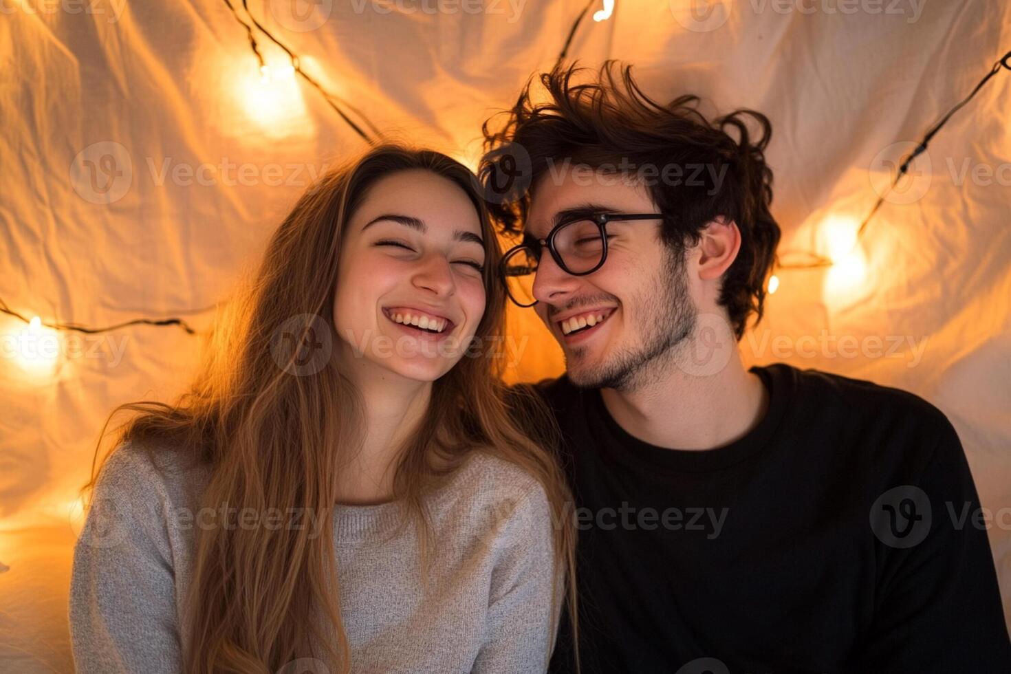 Couple laughing and smiling in front of a string of lights photo