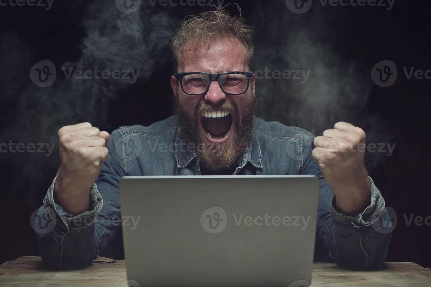 A man with glasses and a beard is sitting in front of a laptop photo