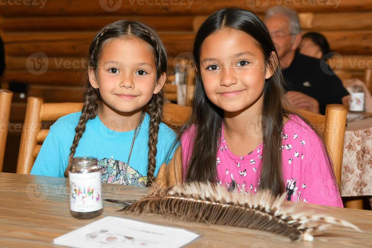 Two young girls pose for a photo at a table with feathers