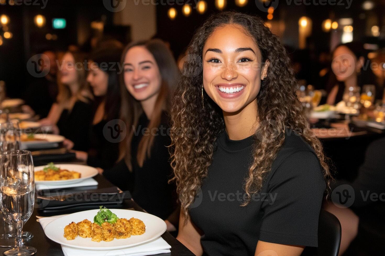 A woman smiles while sitting at a table with food photo