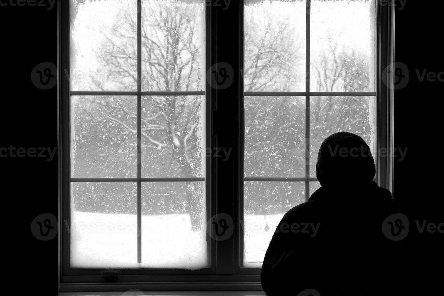A person is standing in front of a window looking out at snow photo