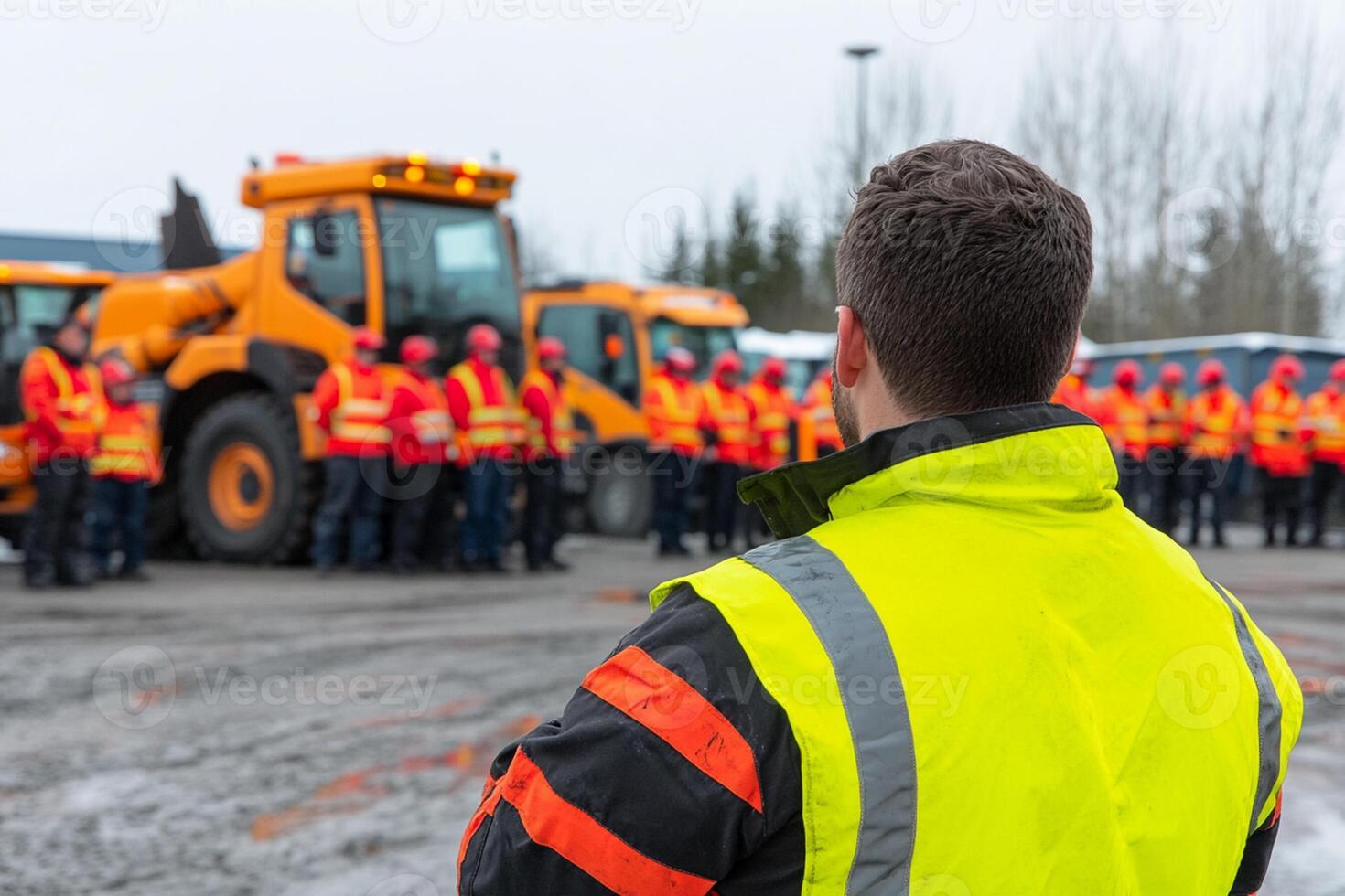 A man in an orange vest and yellow vest standing in front of a group of construction workers photo