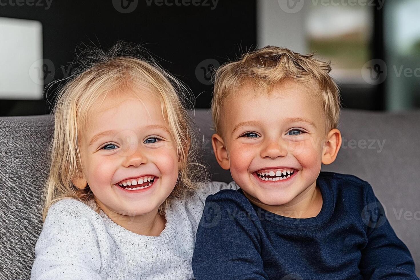 Two young children sitting on a couch smiling photo