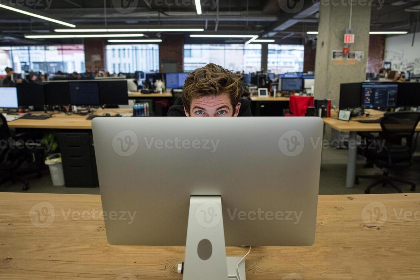 A man is looking at a computer screen in an office photo