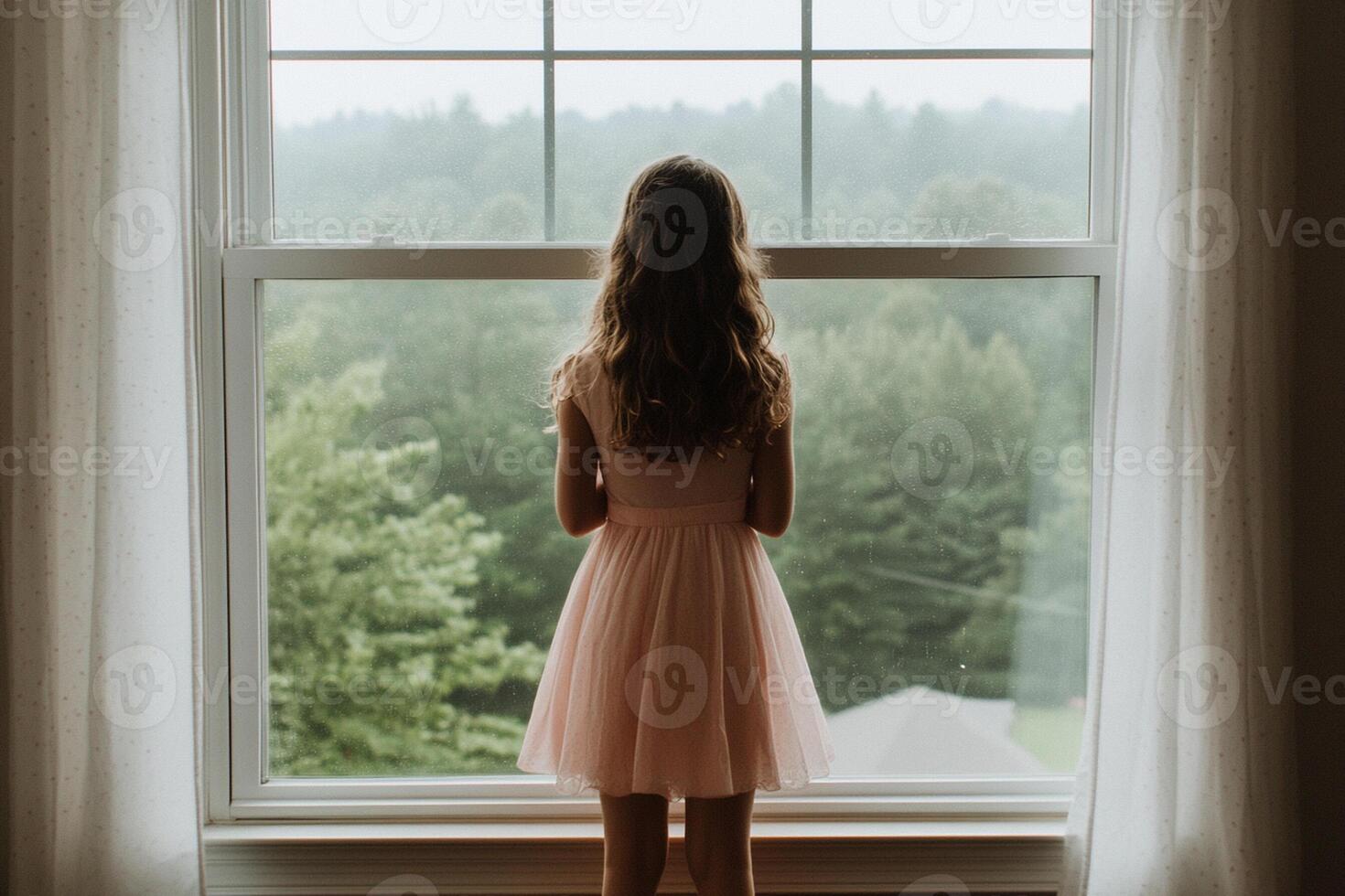 A little girl in a pink dress standing in front of a window photo