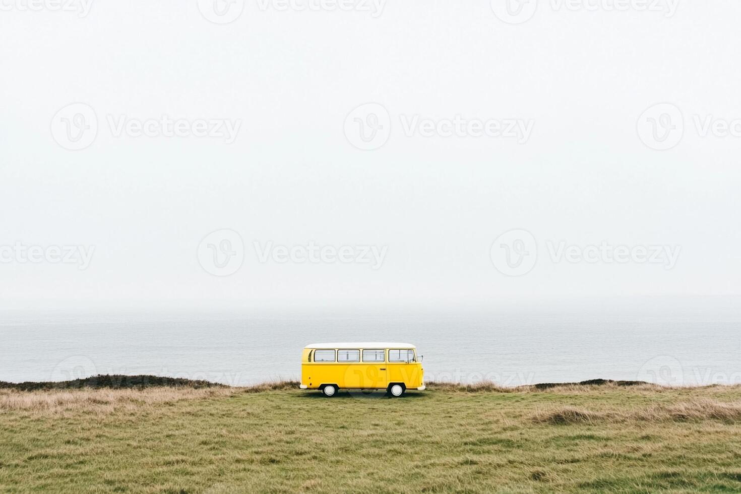 A yellow bus sits on a grassy hill overlooking the ocean photo