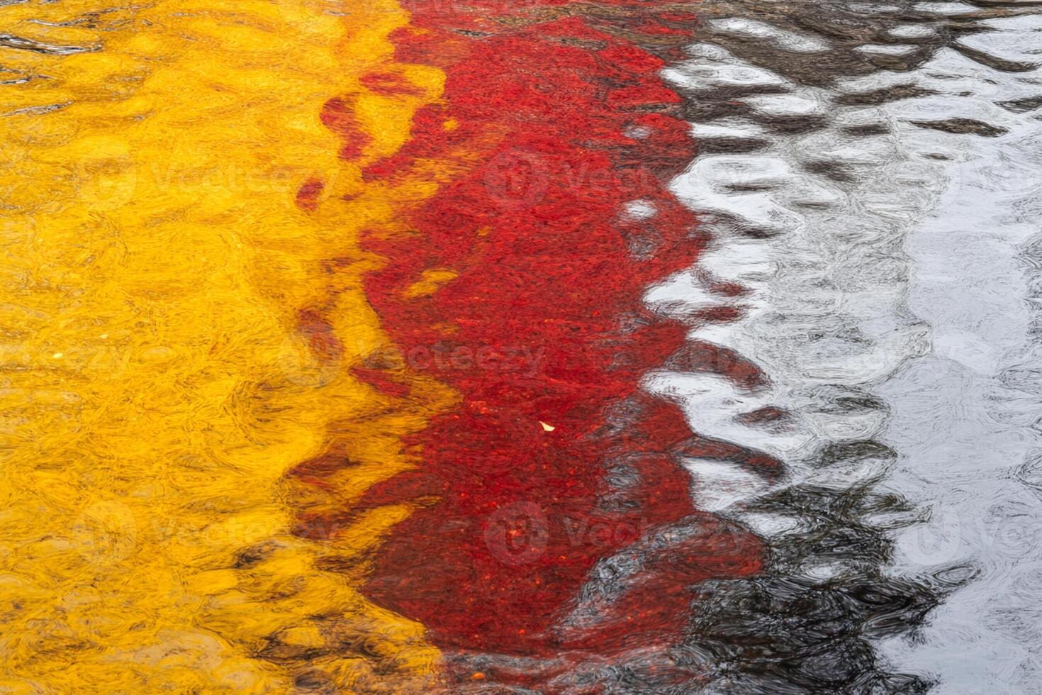 A red, yellow and black umbrella is reflected in a puddle photo