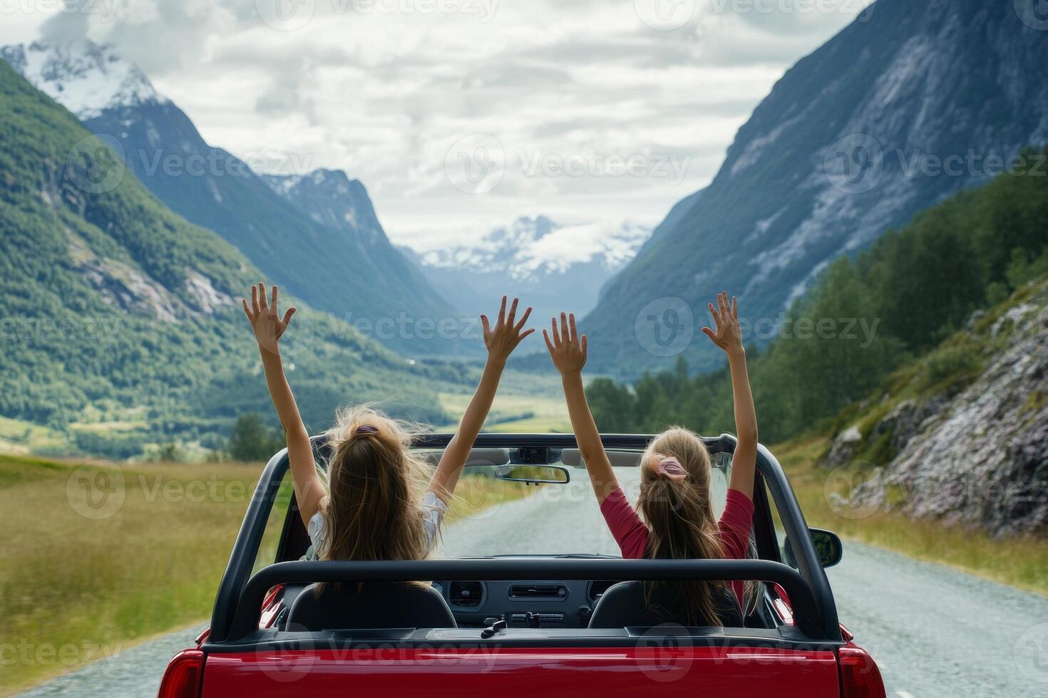 Two girls enjoy a joyful road trip with hands in the air in a scenic mountain landscape photo
