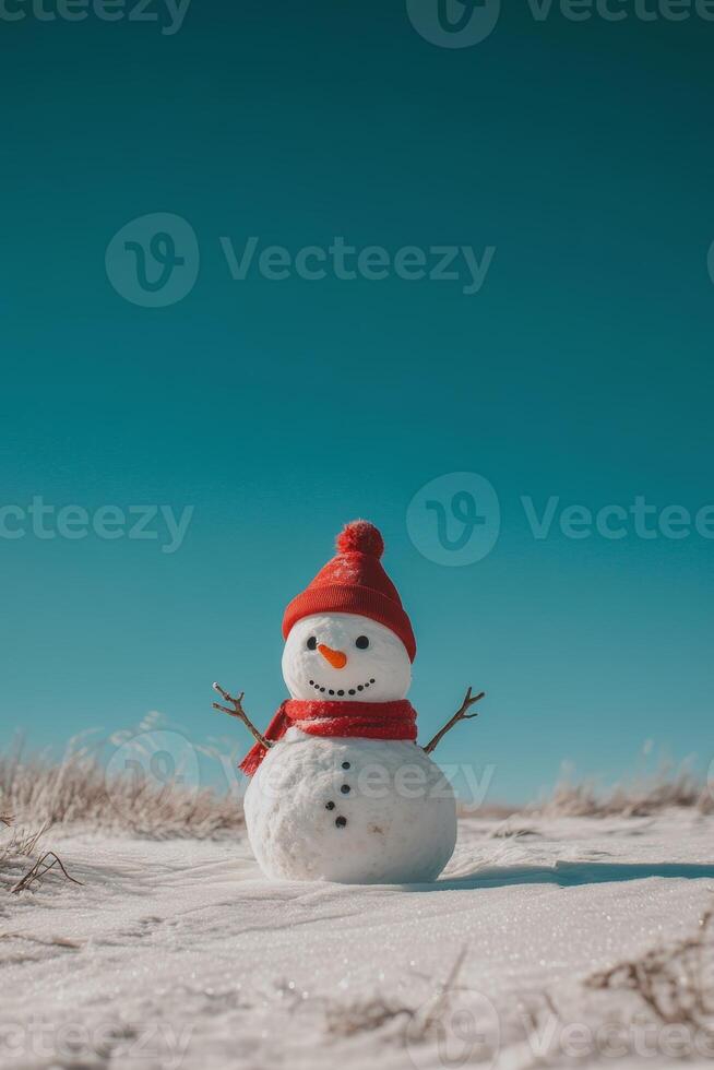 A cheerful snowman wearing a red hat and scarf stands in a snowy field under a bright blue sky with plenty of room for text photo
