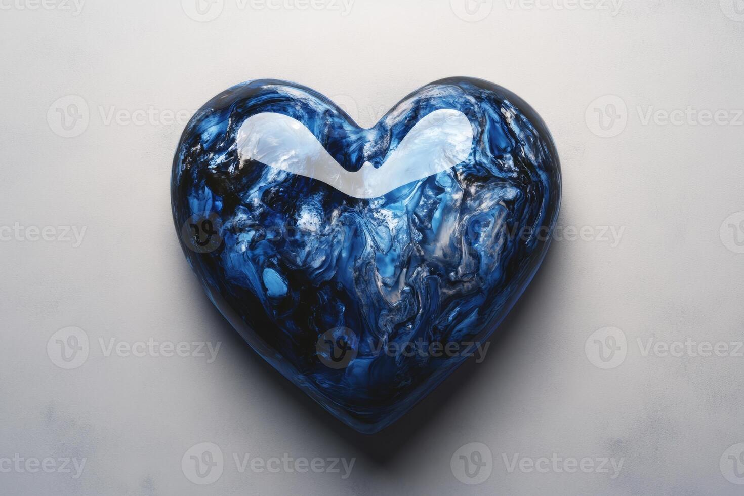 A glossy blue heart resting on a light gray surface, reflecting soft light in an artistic display of color and shape photo