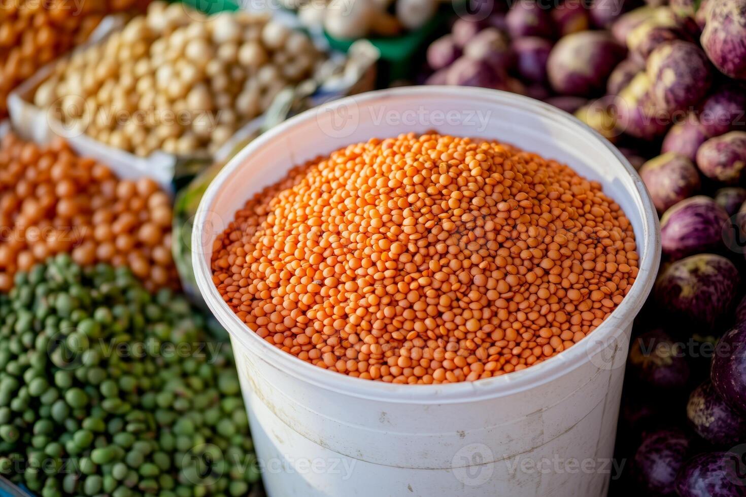 Red lentils in a white bucket at a bustling market surrounded by various legumes and produce photo