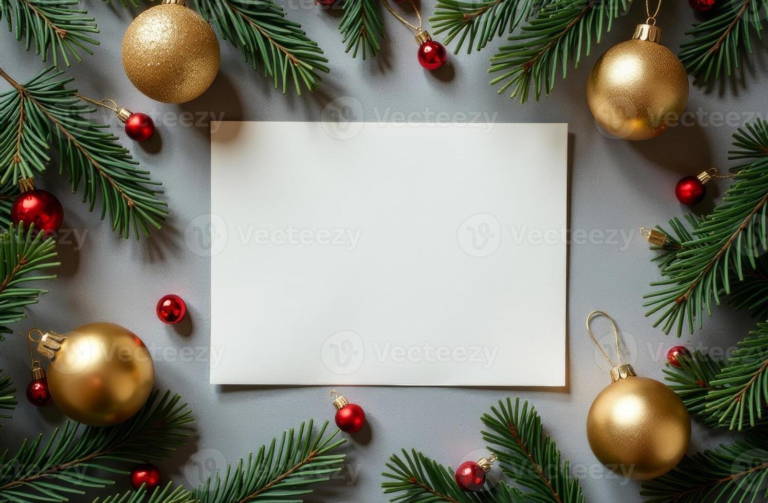 A festive arrangement of pine branches, golden ornaments, and a blank card ready for holiday greetings on a simple gray background photo