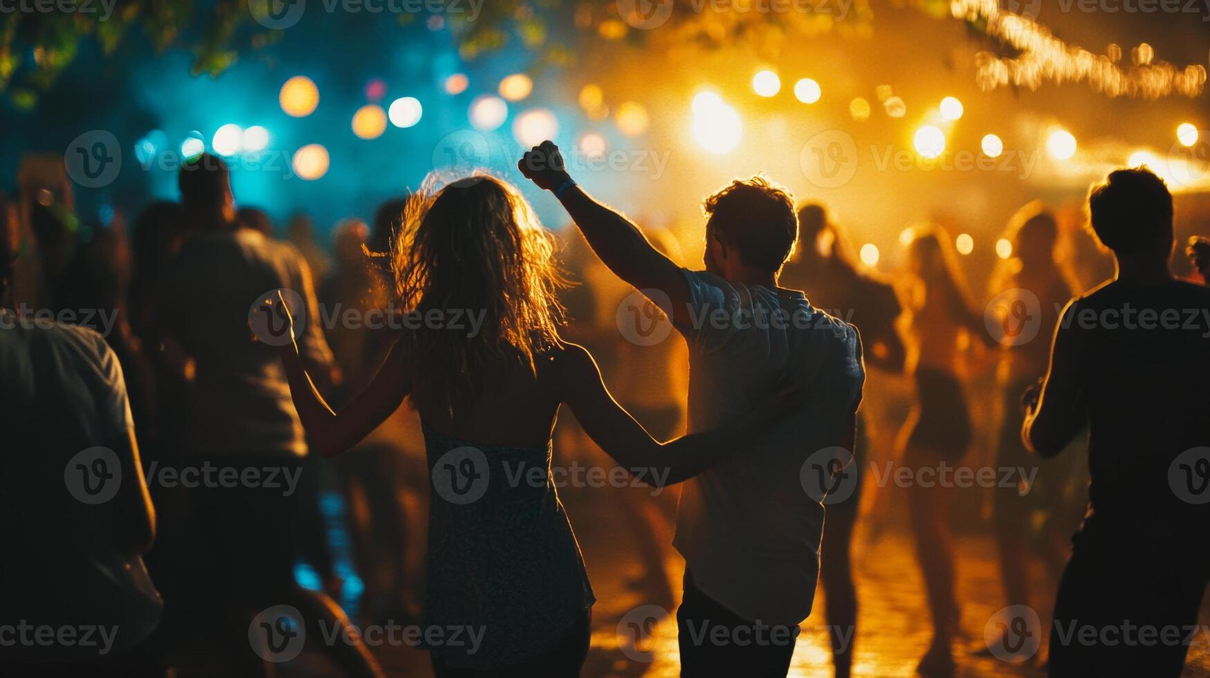 People joyfully dancing together at an outdoor concert party during a lively summer night under colorful lights photo